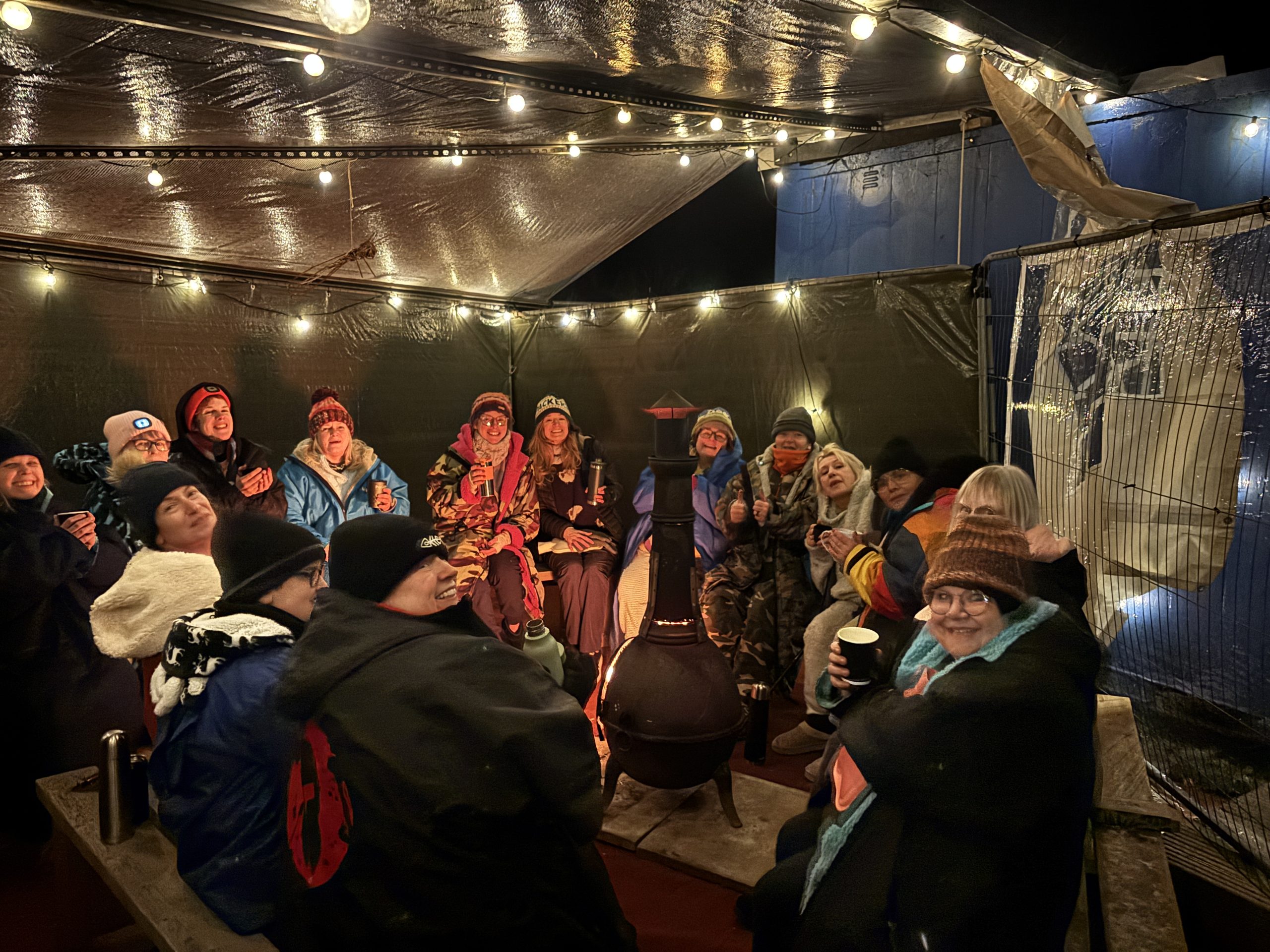 Lakeside swimmers enjoying a cosy winter get-together around the fire pit under fairy lights